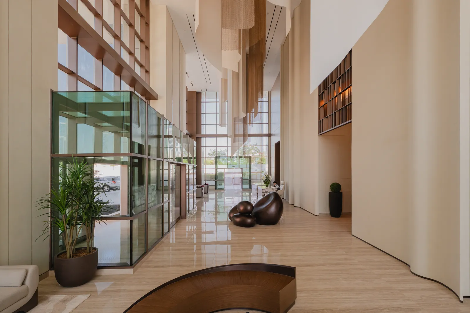 The lobby: a green-tinted glass vestibule with a palm, the crescent bench, the bronze pebble sculpture, a bronze lattice screen high on the wall and curved cream walls