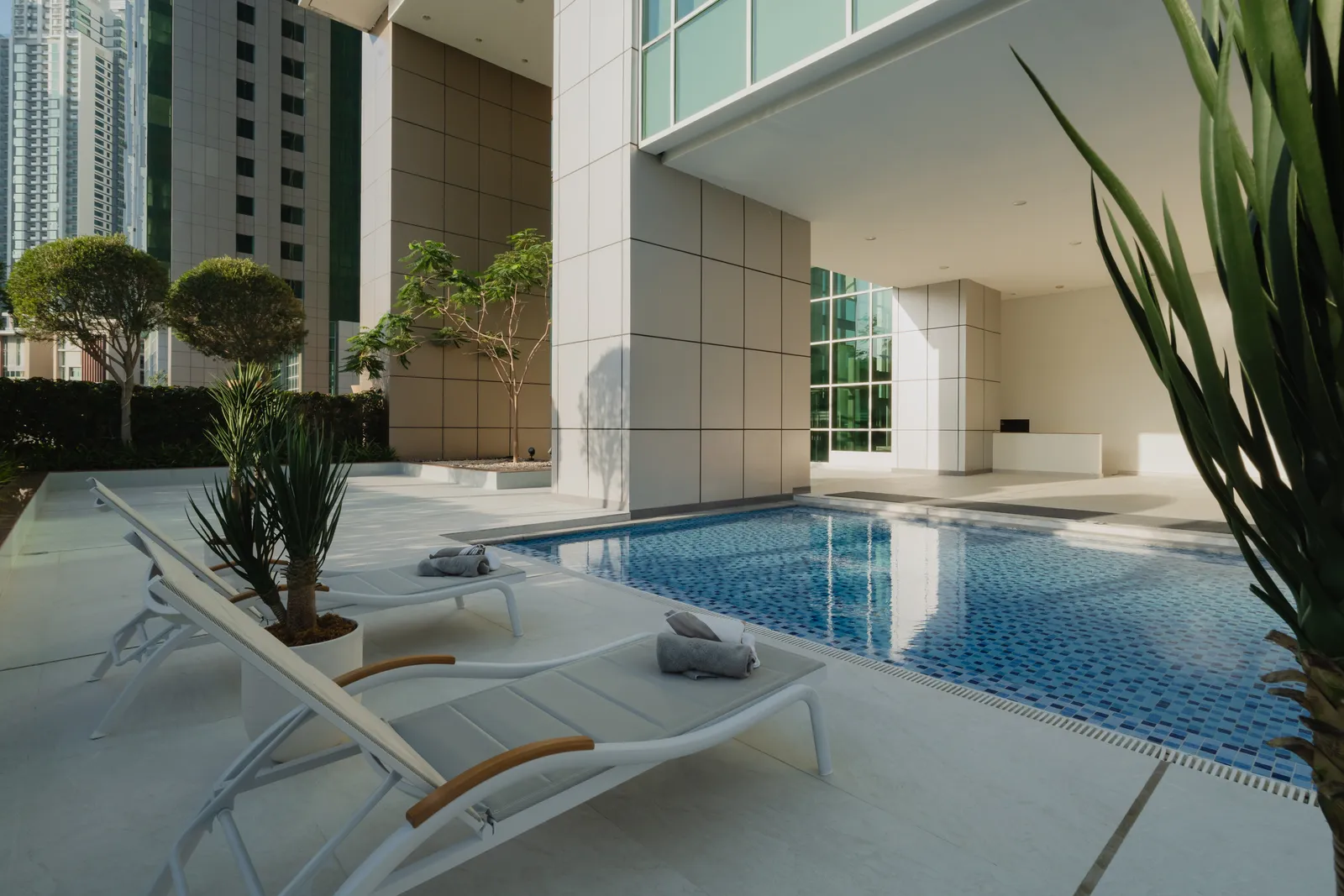 The children's pool at the base of the tower: two loungers with rolled towels, potted palms, the pool and the podium's cream columns, towers above