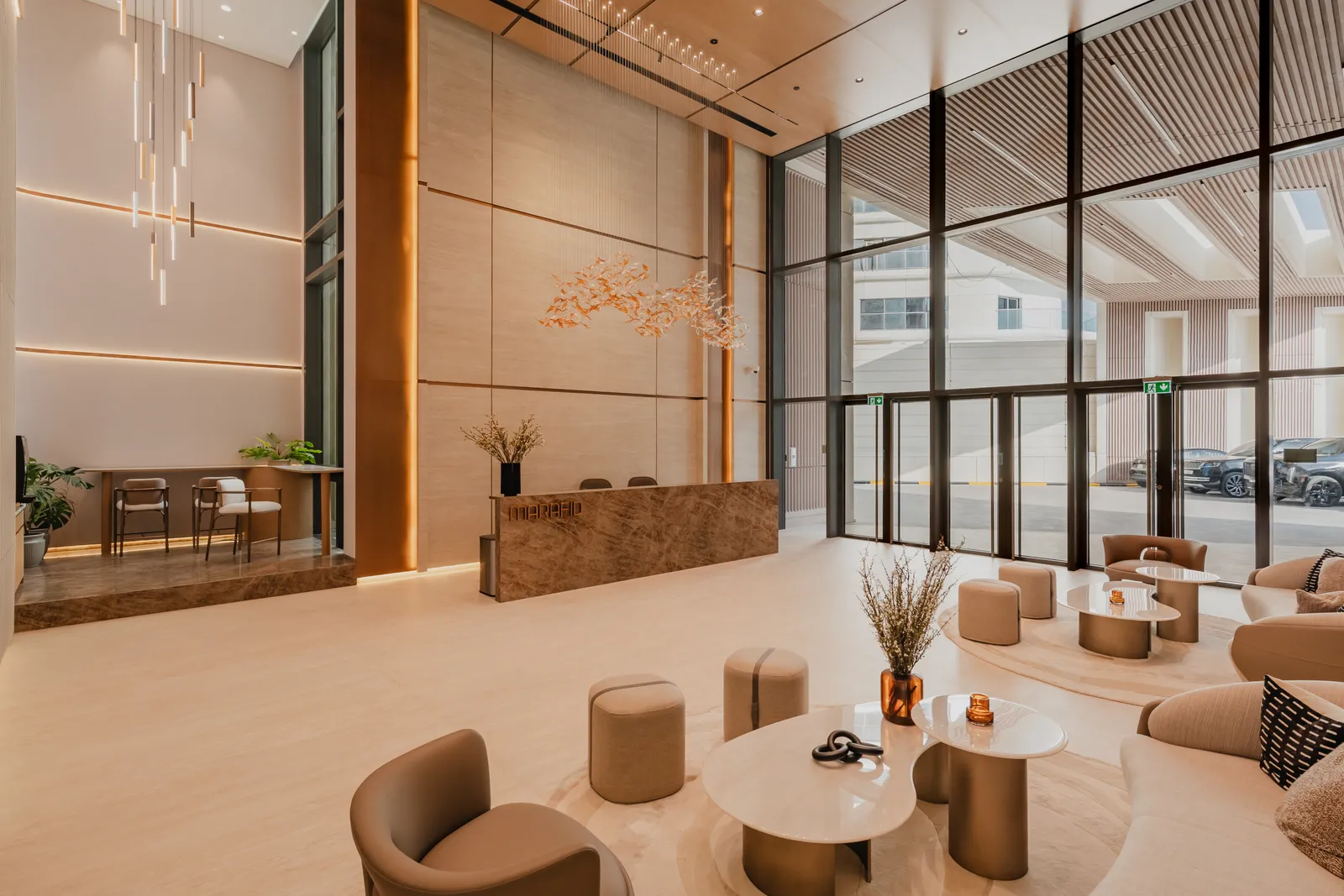 Lobby seating beside the entrance glazing: low cream chairs and pouffes around round tables, the reception desk and gold-leaf artwork in the background